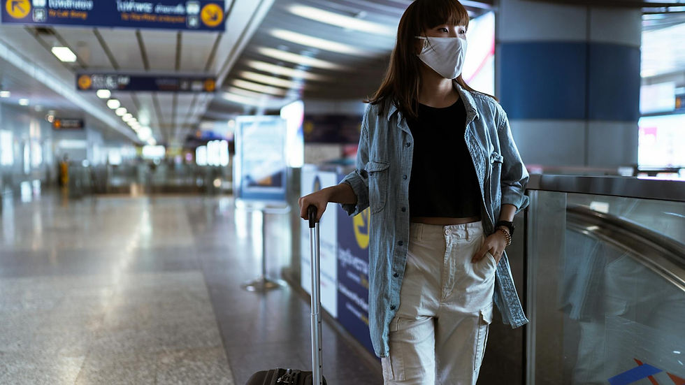 Woman wearing mask and denim jacket in airport terminal with luggage.