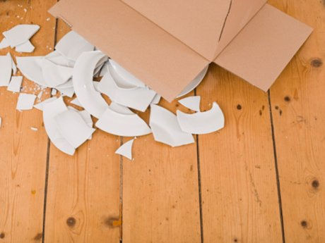 A box fallen on wooden floor planks with glass plates all broken everywhere in sharp pieces
