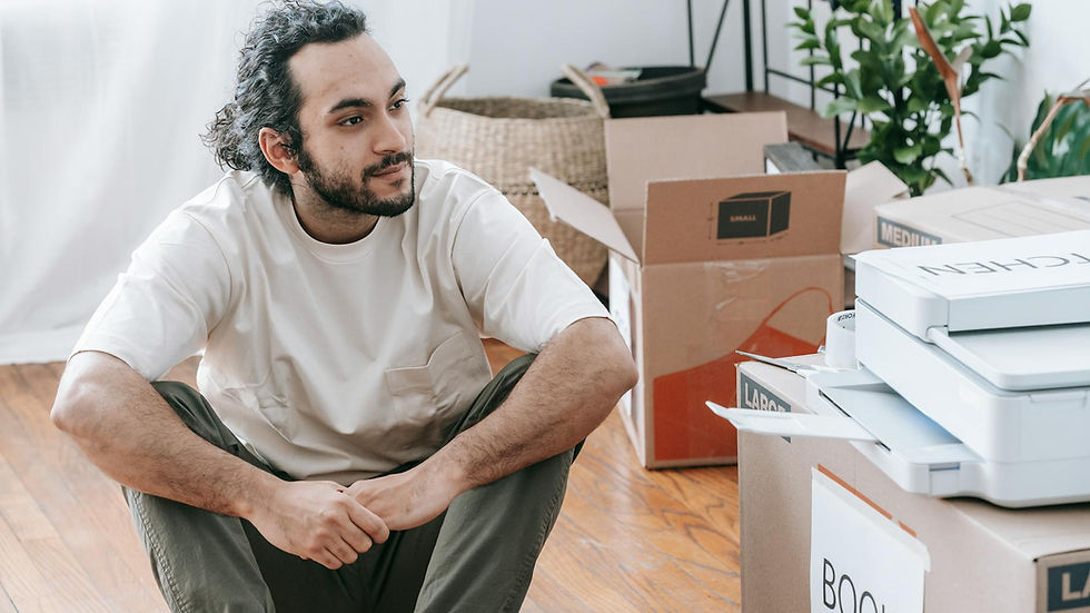 A man sitting on the floor surrounded by boxes, contemplating and organizing during a move.
