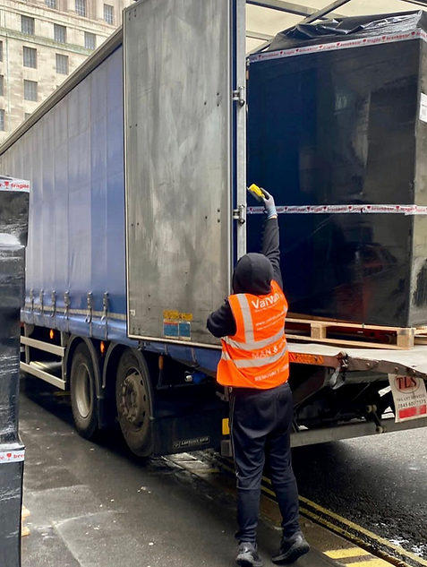 A VaiVan moving company porter mover unloading palleted boxes shrikwarpped fragile tapped goods from a 7.5 tonne lorry using a taillift