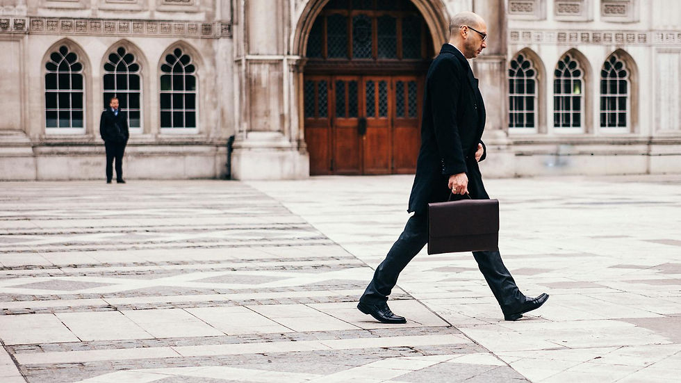 A businessman in formal attire walking past a historic building facade.