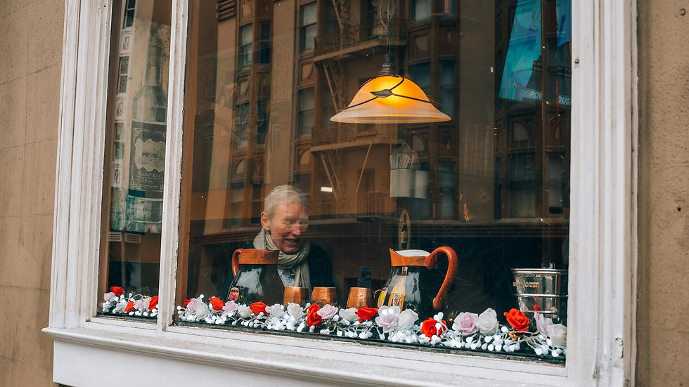 Elderly man relaxing inside a cozy café with decorations. Captured through the window.