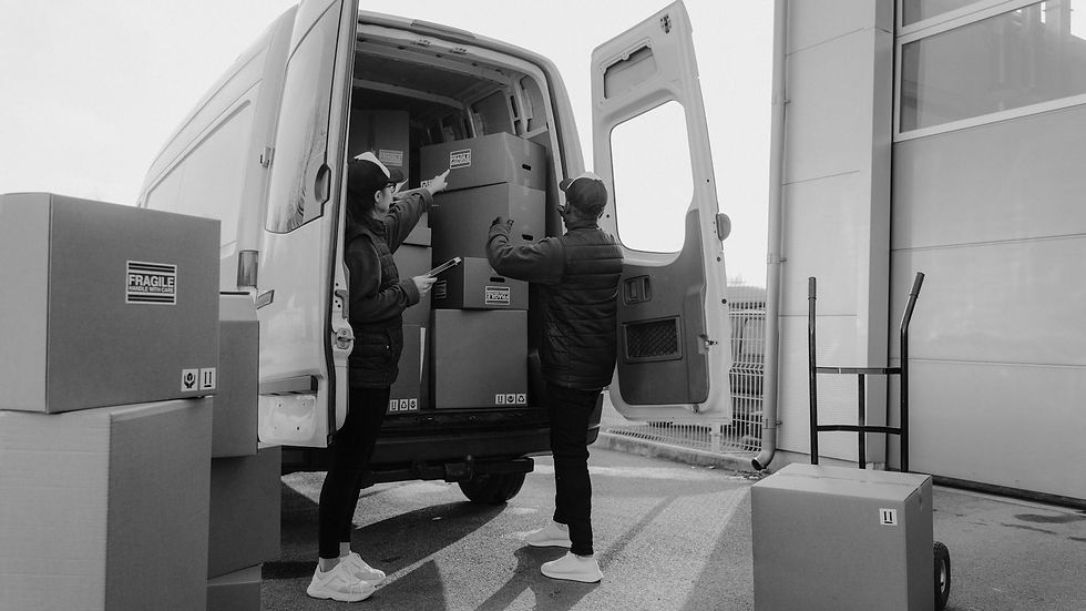 Two couriers loading cardboard boxes into a delivery van outdoors.