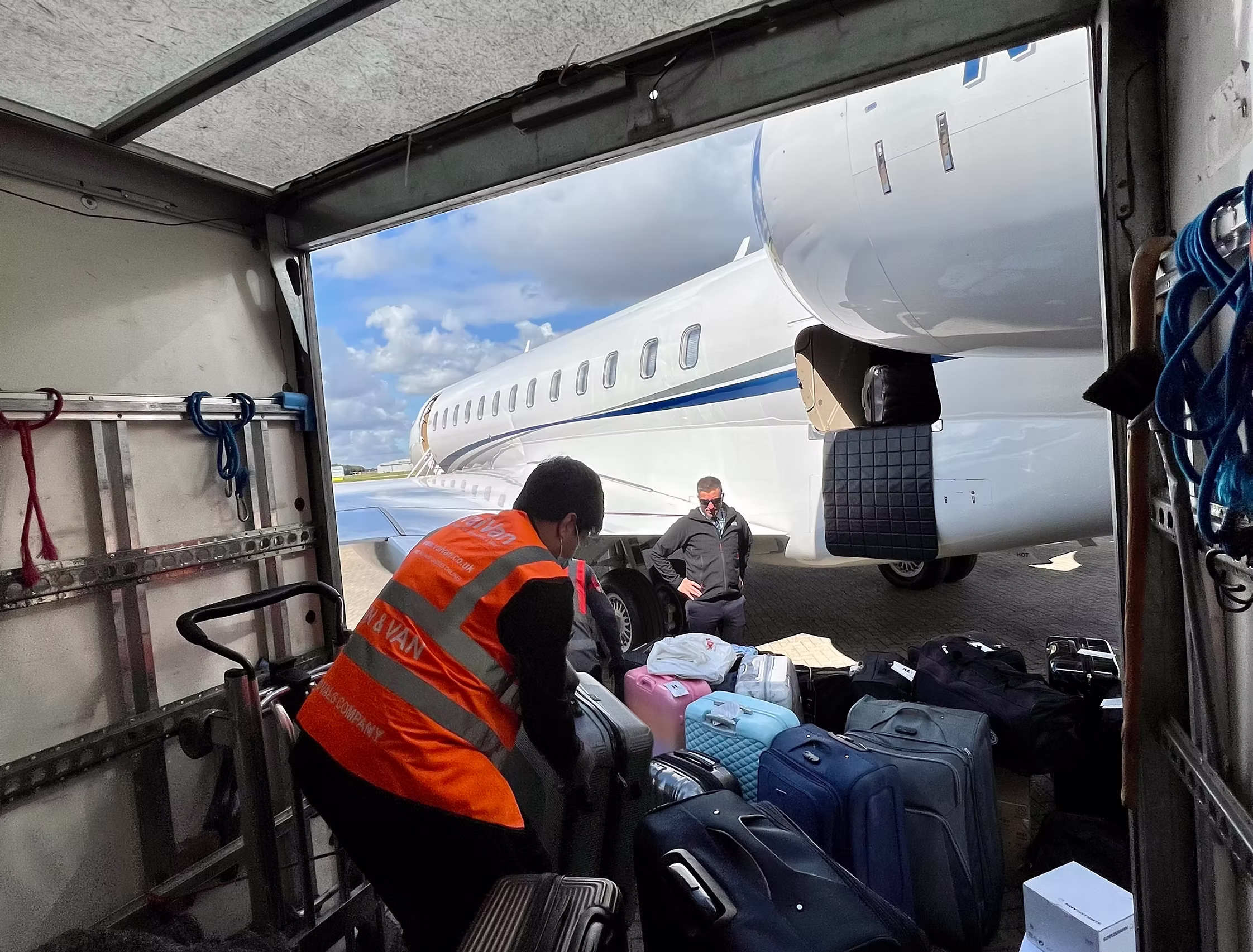 An Airport To Home porter courier unloading bags from the delivery truck holding about 60 suitcases into a private jet for a private client flying from a private hanger luggage transfer service