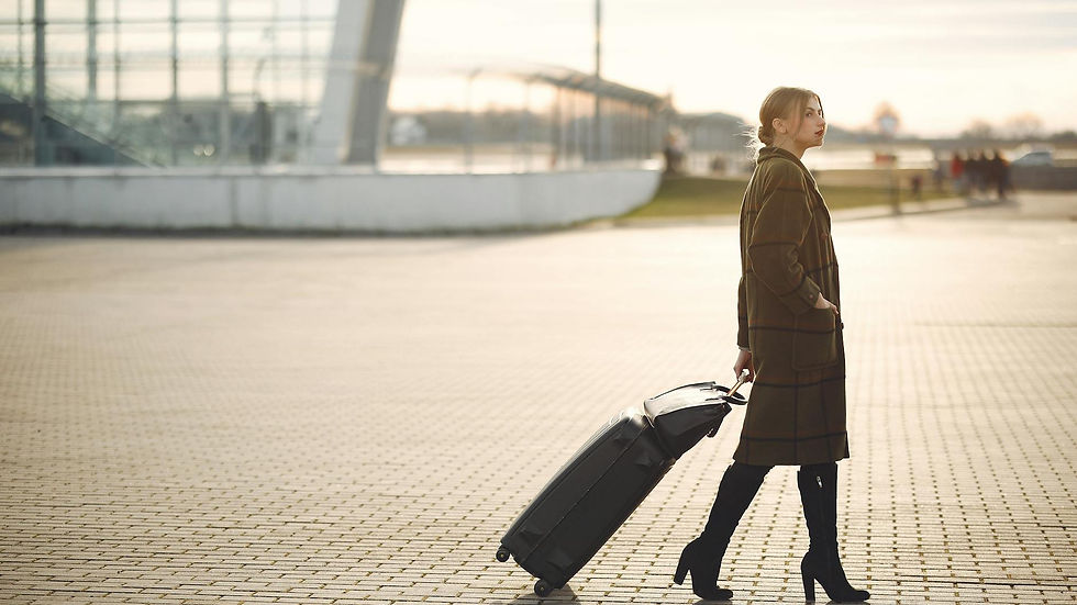 Side view of full length young female traveler in trendy plaid brown coat and high boots with suitcase walking on pavement near modern building on city street in morning
