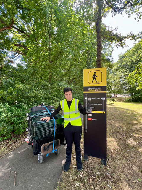 Airport To Home porter posing next to Gatwick Airport South Terminal signage walkway with a trolley full of bags