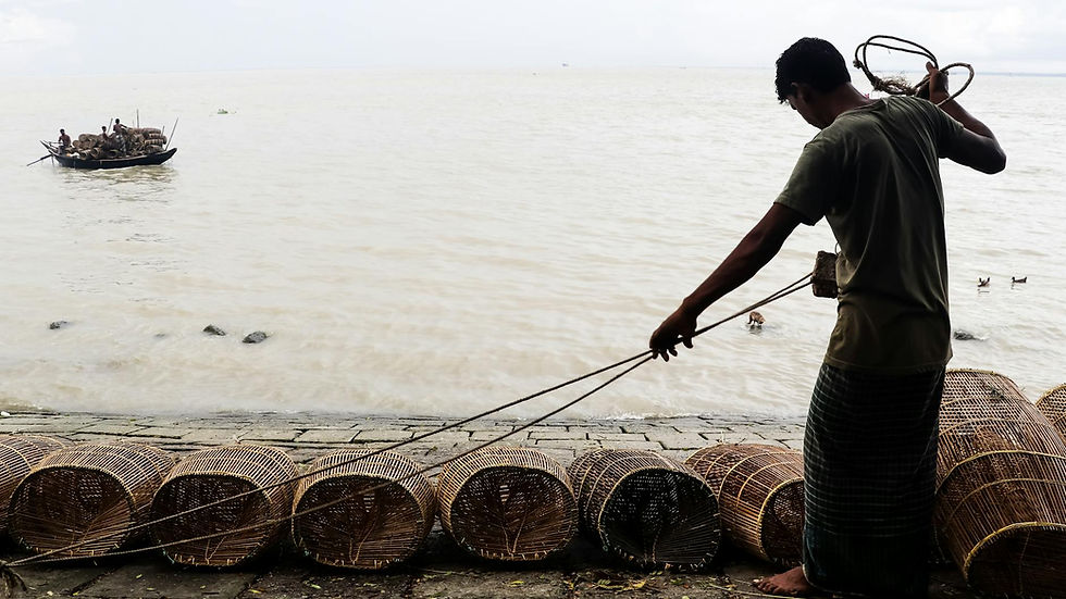 Silhouette of a fisherman preparing bamboo fishing cages by a serene riverside.