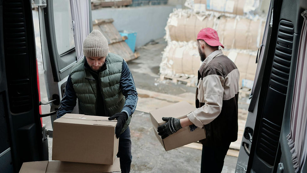 Two men unloading cardboard boxes from a delivery van in an industrial area.