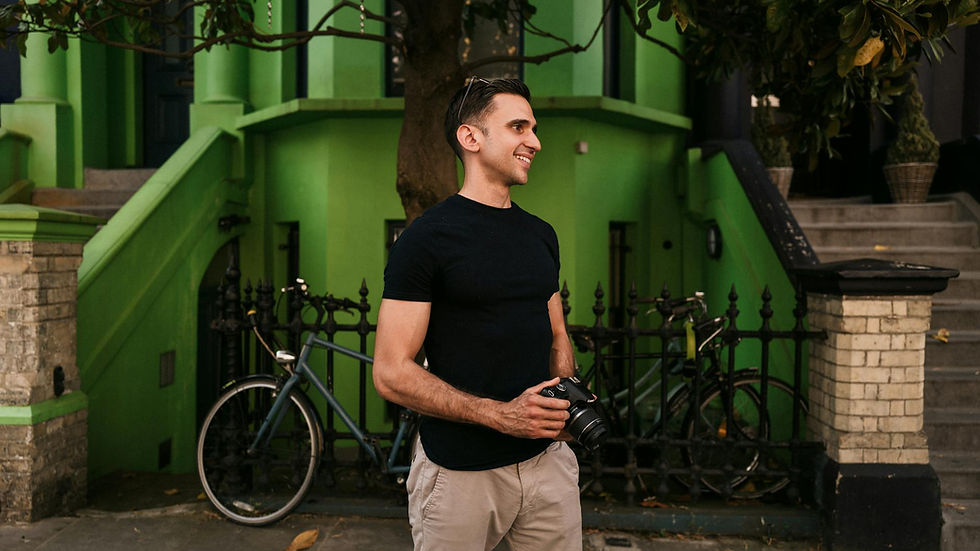 A smiling man with a camera in an urban London setting with vibrant green buildings.