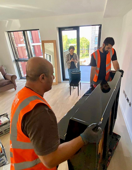 2 VaiVan porter movers from VaiVan moving company installing and moving an upright black shiny piano for a customer in their new apartment-flat home