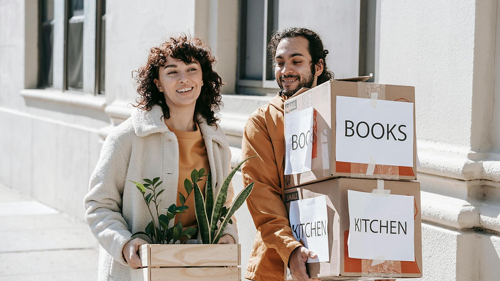 A smiling couple carrying boxes and plants while moving into a new urban home.