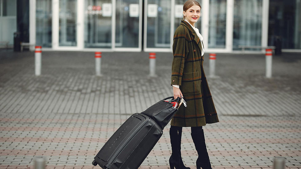 Full length of smiling female manager in stylish coat walking with suitcase and bag while traveling on business trip smiling away