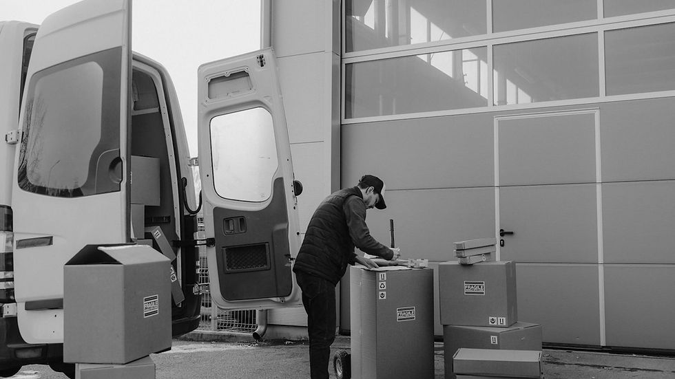 Monochrome image of a courier managing packages outside a warehouse, illustrating logistics workflow.