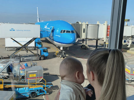 Moeder houdt haar baby vast terwijl ze samen uitkijken op een KLM-vliegtuig bij de gate op de luchthaven