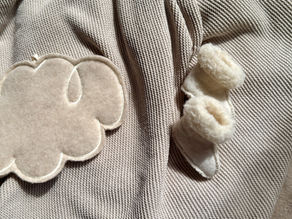 Zachte beige babydeken met wollen wolkdecoratie en wollen baby slofjes, perfect voor een warme en comfortabele babykamer