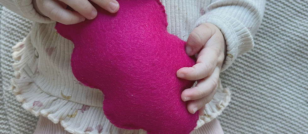 Baby houdt een felroze vilten wolkvorm vast, een zacht speeltje dat de tastzin stimuleert.