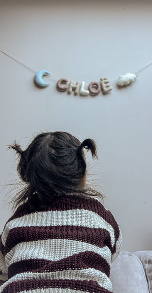 Thumbnail: Jong kind kijkt naar een muur waar een wolvilten handgemaakte slinger hangt met een maan, de naam Chloë en een wolk