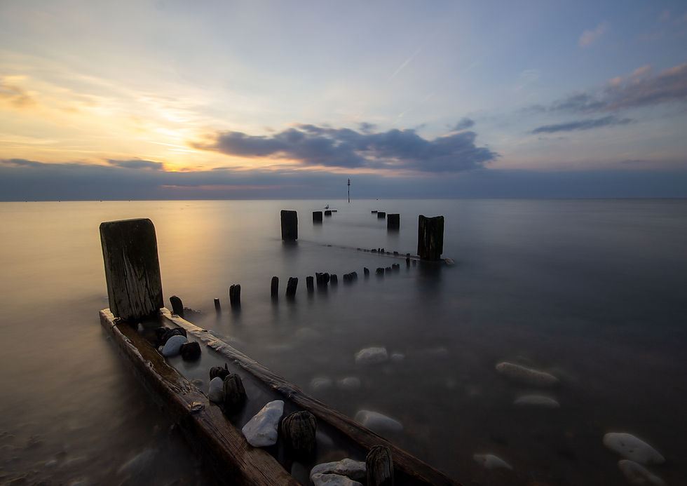 Weathered wooden posts create striking leading lines, guiding the eye to the horizon, where the sea meets the soft glow of the evening sky.