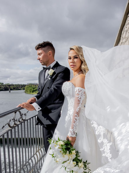 Bride with blonde Hollywood waves and glamorous wedding makeup posing with her groom beside the water.