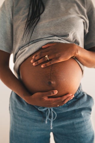Pregnant mother holding her baby bump with hands and wedding ring visible during studio maternity session