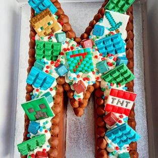 A minecraft themed M shaped cake with green and blue mini chocolate bars and minecraft themed tiles.