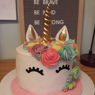 A round white cake depicting a unicorn head with pastel coloured swirls of buttercream for the mane and a gold horn and gold accented ears