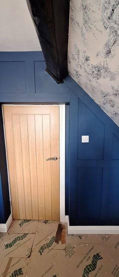 Showing repaired wooden door set into blue painted feature wall with roof slope to the right