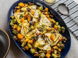 Ravioli with roasted vegetables on a dark blue plate, set on a striped tablecloth. Creamy sauce topping, mix of vibrant green and orange.