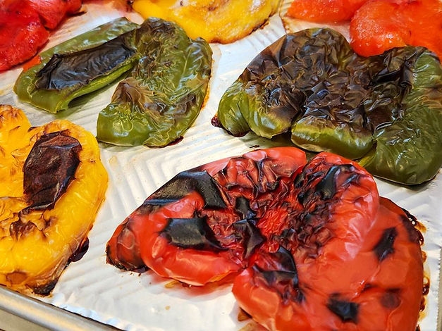 Roasted red, green, and yellow bell peppers rest on a shiny baking tray, showing charred and vibrant colors with a savory appeal.
