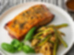 Grilled salmon with pasta, fresh vegetables, basil garnish, and savory sauce.