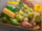 Corn, tomatillos, lime, jalapeño, shallot, garlic, cilantro on a tray with cumin, oregano, and citrus juicer. Checkered tablecloth background.