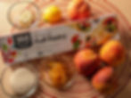 Puff pastry box, peaches, lemon, butter, sugar, and jam on a red and beige baking mat. Emphasis on baking ingredients.