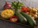 Fresh vegetables on a checkered tablecloth, including corn, red onion, zucchini, potatoes, basil, tomatoes, and minced garlic. Warm lighting.