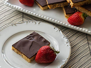 Chocolate-covered square on a decorative plate with a strawberry. More squares and strawberries on a platter. Zigzag table pattern.