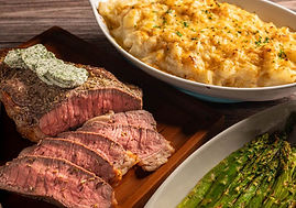 Sliced steak with herb butter, baked mashed potatoes, and grilled asparagus on wooden table; warm, appetizing dining ambiance.