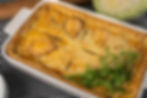 Golden pastry pie with leaf-shaped crust decorations, garnished with dill on a black-and-white checkered cloth. Cabbage in the background.