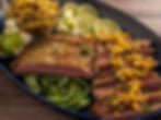 Sliced steak on a platter topped with corn salsa, surrounded by lime slices, tomatillos, and cilantro. The mood is appetizing and inviting.