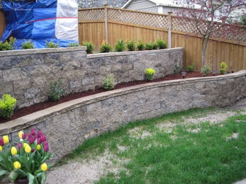 beautiful stone retaining wall with flower and shrub garden built in