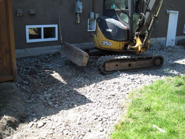Excavator removing a cracked and broken concrete patio slab before paver installation in Victoria BC