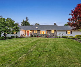 Twilight exterior of 5 Hedges Road in Warwick, NY, featuring a stone-accented ranch home, expansive front lawn, mature trees, manicured landscaping, and warmly lit windows.