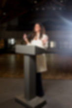 Kathleen Boyle Wrigley, Author & Speaker, standing at a podium speaking excitedly.