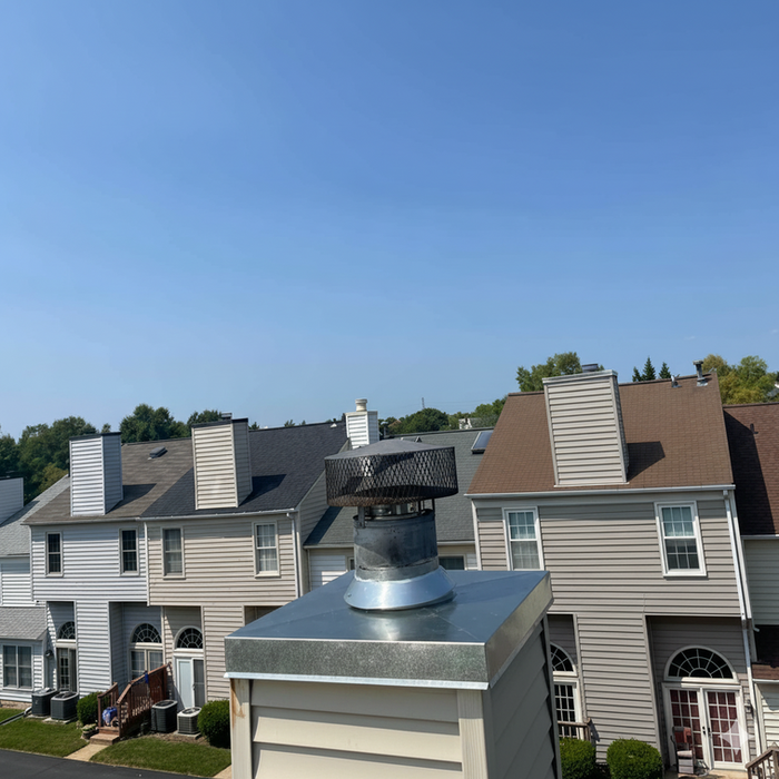 Prefab metal chimney with a newly installed galvanized steel cap by ACD Chimney. The photo shows a townhouse roofline and expert installation service ensuring chimney safety and weather protection in Maryland.