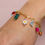 Thumbnail: Gold  bracelet displayed on a wrist that has various charms such as colorful beads,a  daisy, moon, etc.