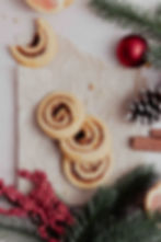 Cinnamon swirl cookies on parchment paper surrounded by holiday decor. One of the four cookies has a bite taken out of it.