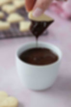 Heart shaped butter cookie being dipped half way in melted chocolate.