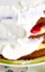 close-up of the layers of cake, pasty cream and cherries being covered in whipped cream.