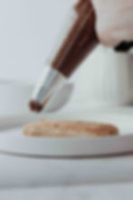 A side angle shot of chocolate mascarpone being piped onto lady fingers.