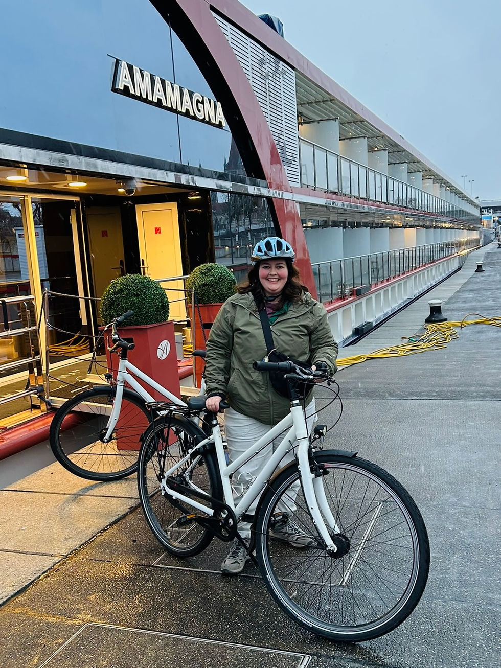 Person in a helmet holding a white bike on a dock beside the AMAMAGNA ship. Overcast sky, damp pavement, and green jacket.
