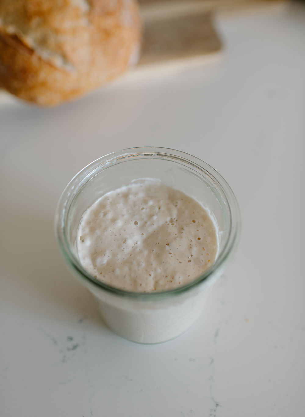 Sourdough starter in jar, bread in background