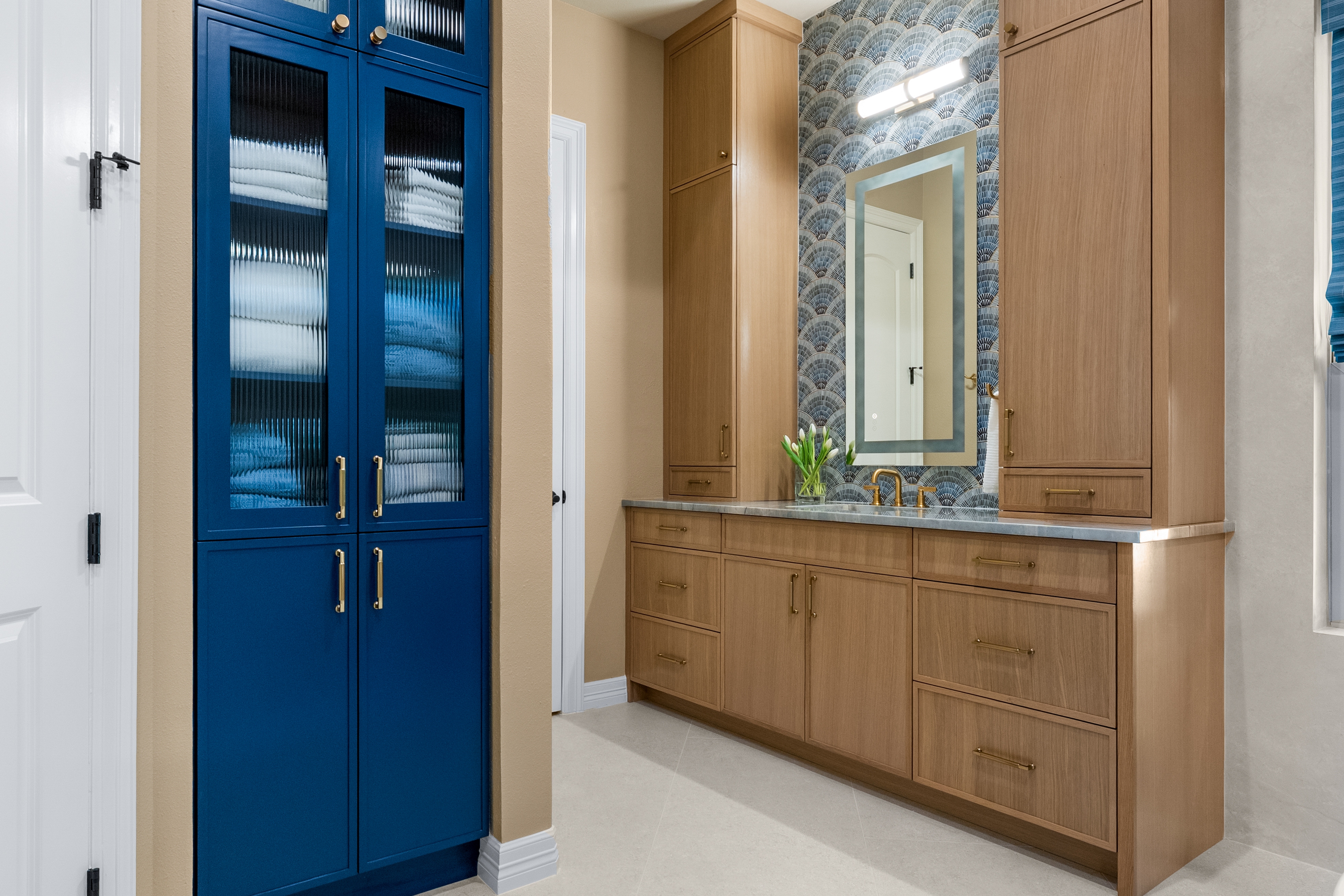 Custom built-in storage in a Cypress, TX home — a floor-to-ceiling blue glass-front linen cabinet beside white-oak storage towers, built by Artosa IDC.